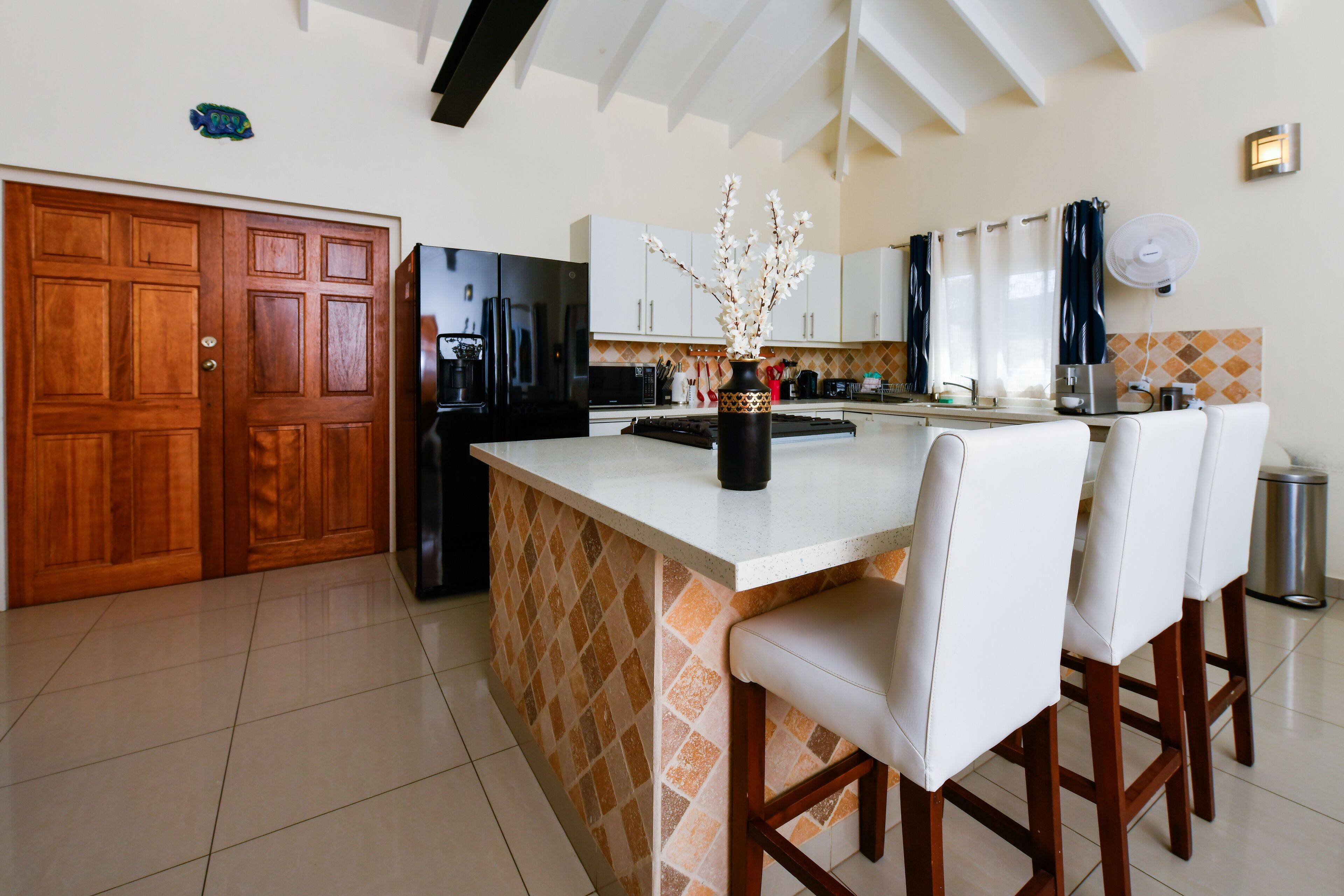 A modern kitchen with a large island, white bar stools, and a wooden door.