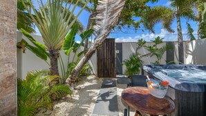 A private outdoor area with a hot tub, a wooden table, and tropical plants. - Swiss Paradise Aruba (Noord)