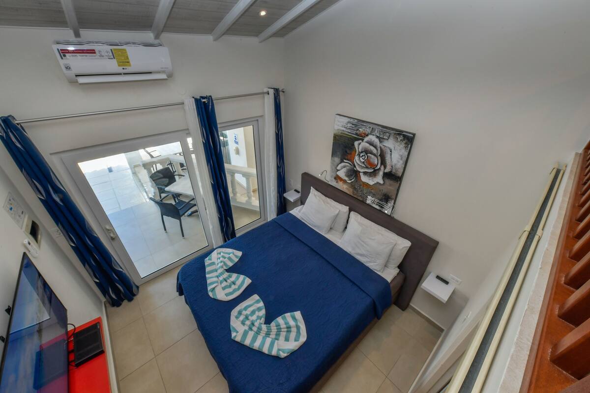 A bedroom with a bed, a painting, a window with curtains, and a view of the outside.
