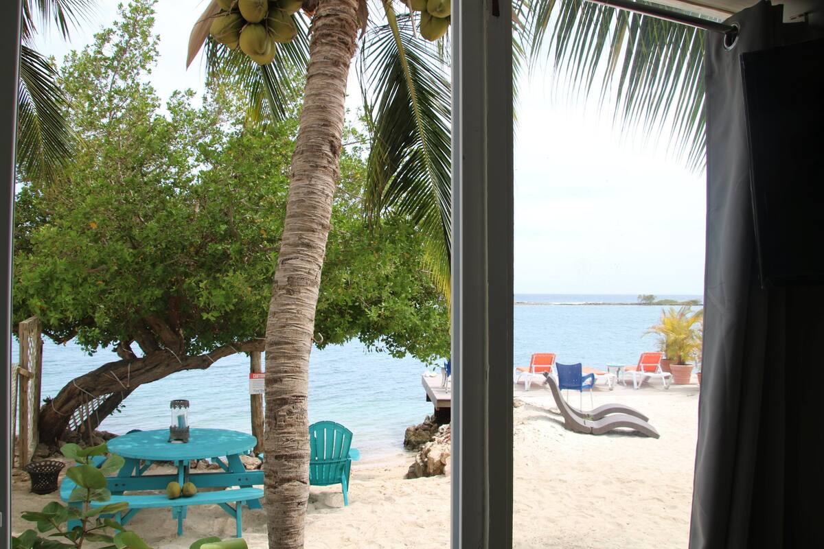 Vista de la playa con una mesa y sillas, palmeras y cielo despejado.