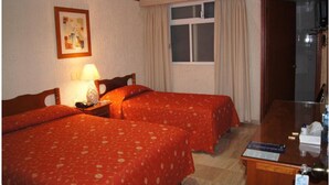 A hotel room with two beds, a desk, a ceiling fan, a window with curtains, and a painting on the wall. - Hotel Veracruz (Oaxaca)
