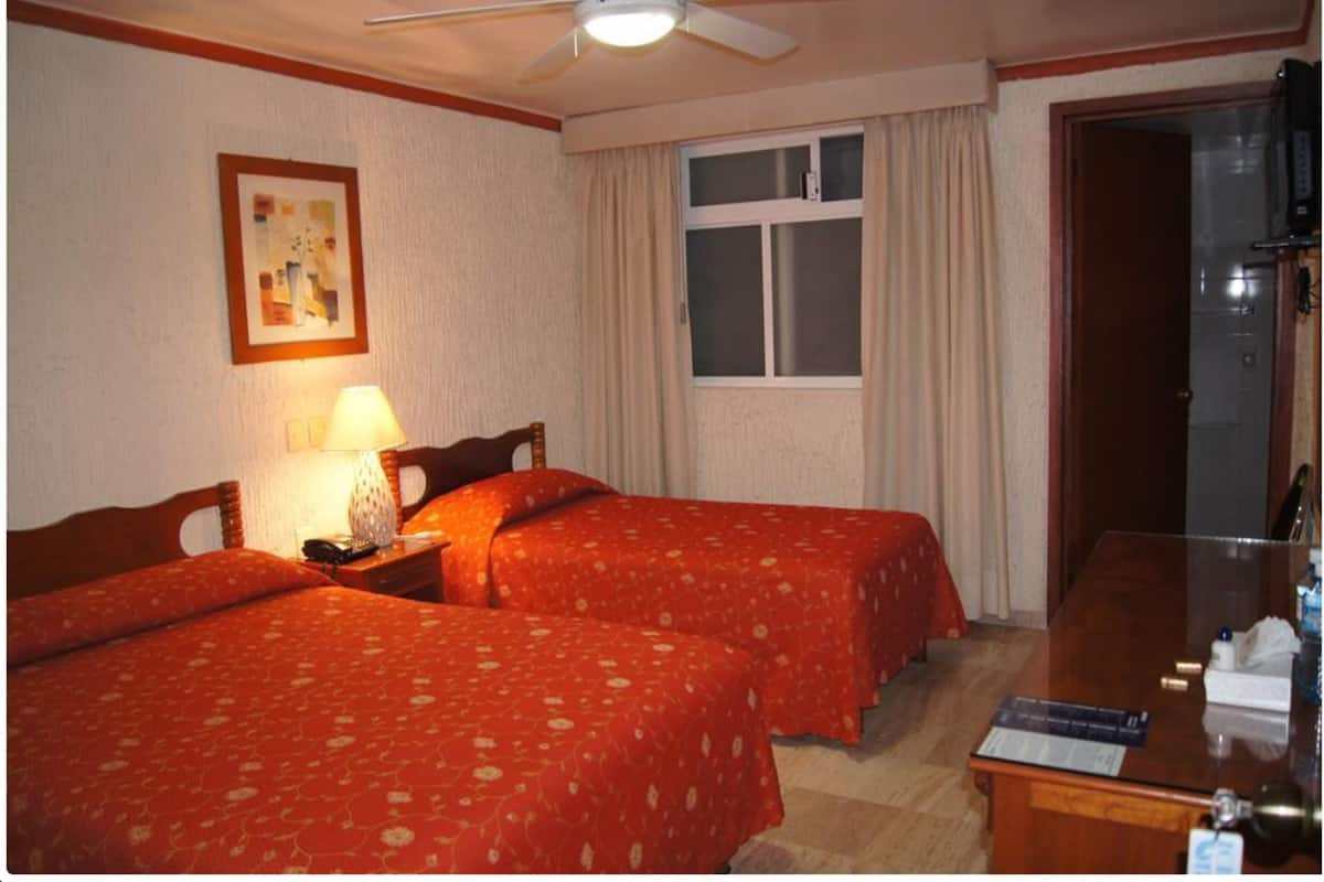 A hotel room with two beds, a desk, a ceiling fan, a window with curtains, and a painting on the wall.