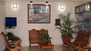 A lobby with wooden furniture, a painting, a television, and potted plants. - Hotel Veracruz (Oaxaca)