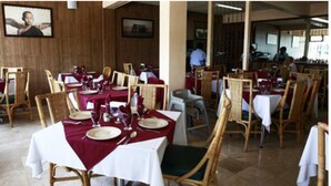 A restaurant with wooden walls, tables set with white tablecloths and red napkins, and wicker chairs. - Hotel Veracruz (Oaxaca)