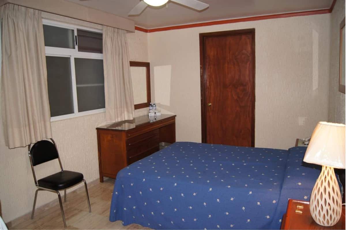 A bedroom with a bed, a wooden dresser, a chair, a window with curtains, and a door.