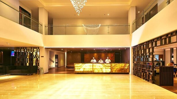 A spacious lobby with a reception desk, a chandelier, and a high ceiling.