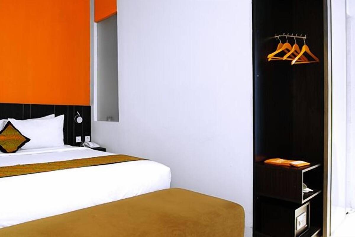 A modern hotel room with a large bed, a black headboard, and a wardrobe with hanging clothes.