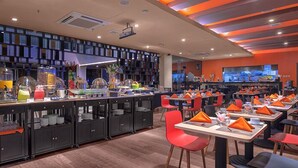A modern restaurant with a long counter, red chairs, and a variety of food items displayed.