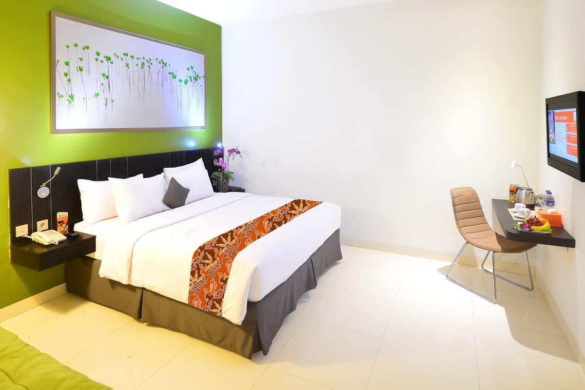 A modern hotel room with a bed, bedside table, chair, and a wall-mounted TV.