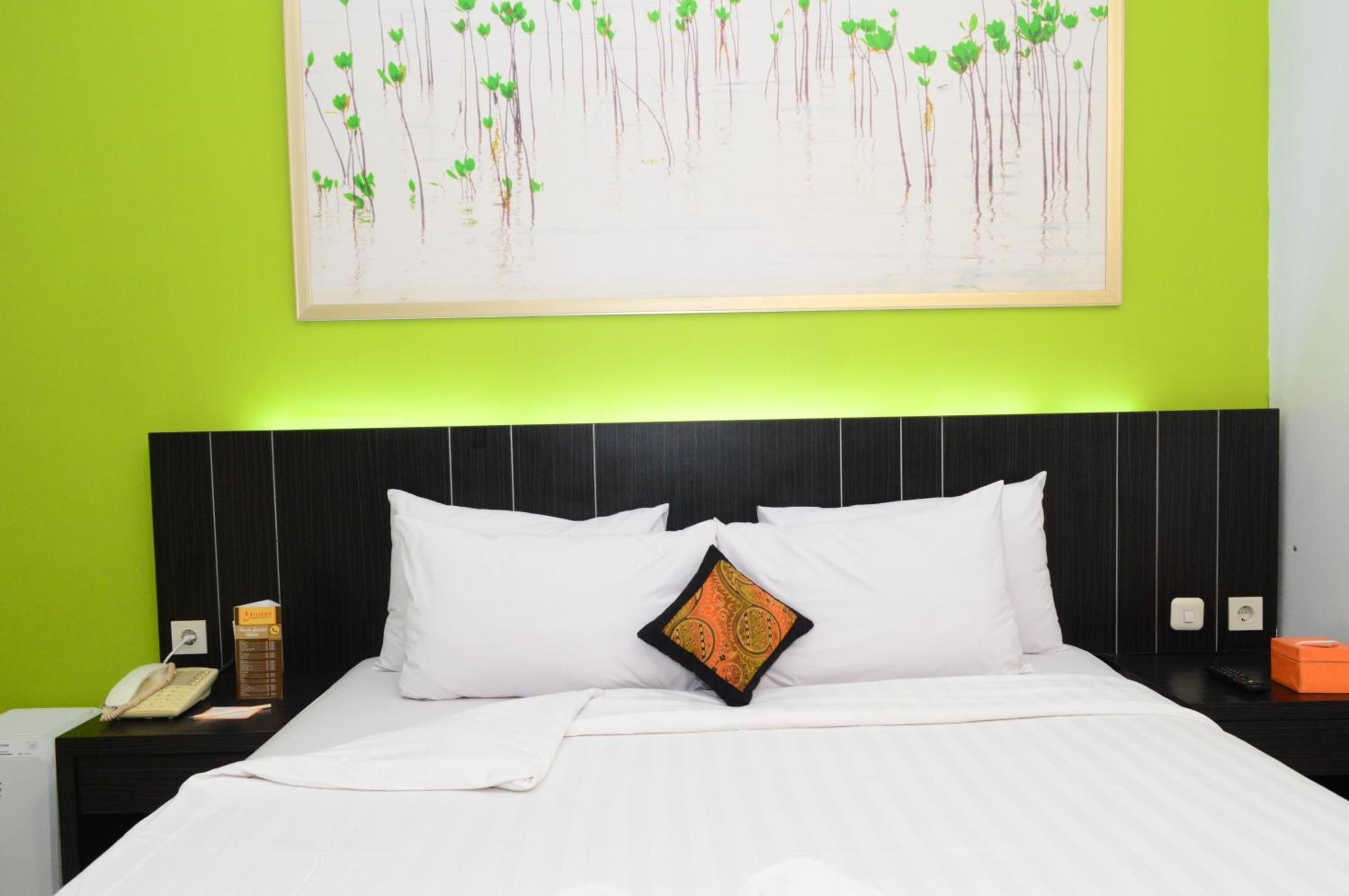 Habitación de hotel con cama, almohadas blancas, mesita de noche con teléfono, control remoto y una pequeña caja naranja.