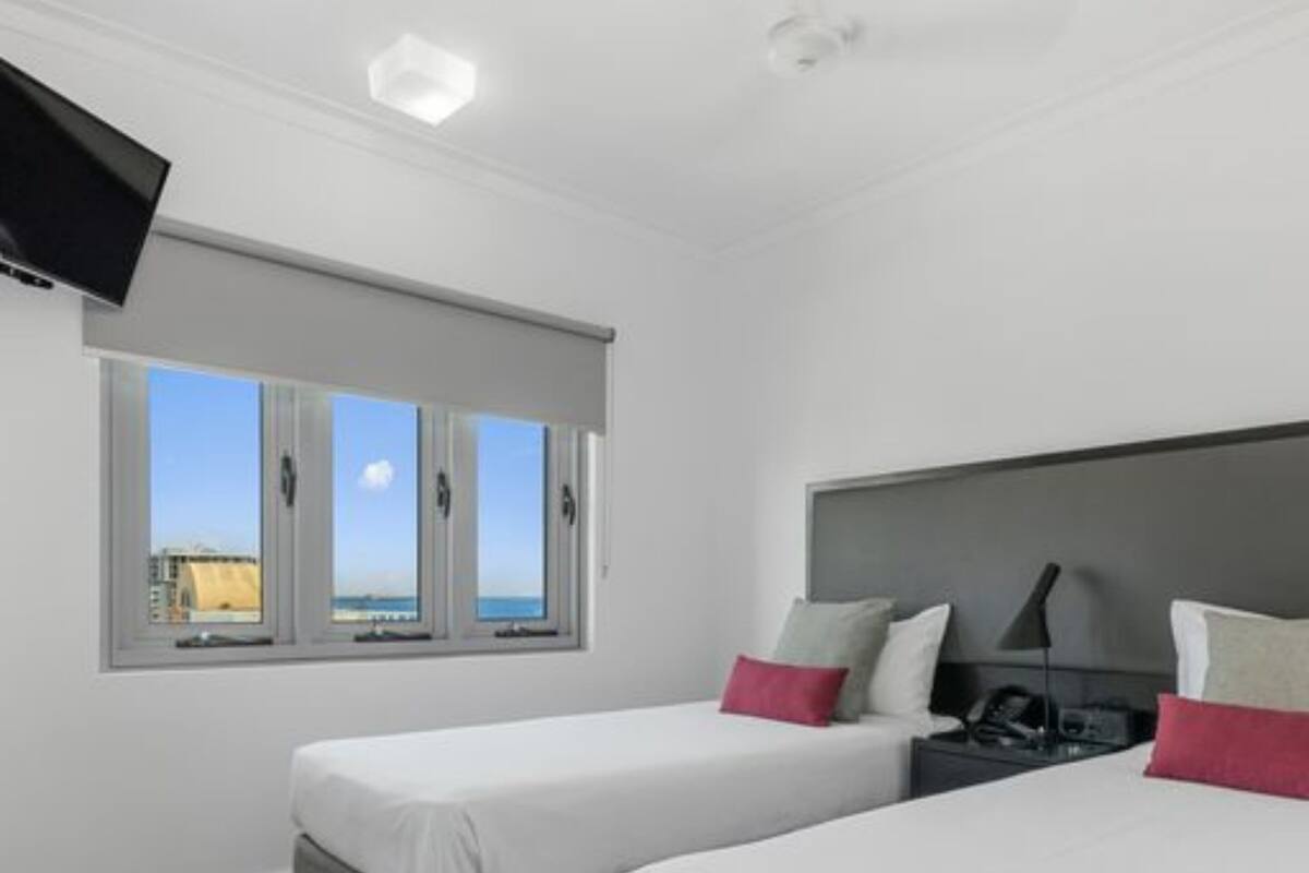 A hotel room with two beds, a TV, a nightstand, and a window with a city view.