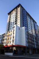 Um edifício alto com vários andares, design arquitetônico moderno e uma entrada imponente com fachada de vidro.