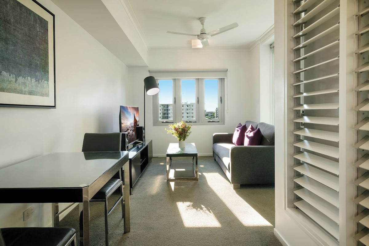 A modern living room with a glass-top table, a sofa, a TV, and a ceiling fan.