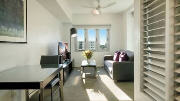 A modern living room with a glass-top table, a sofa, a TV, and a ceiling fan.