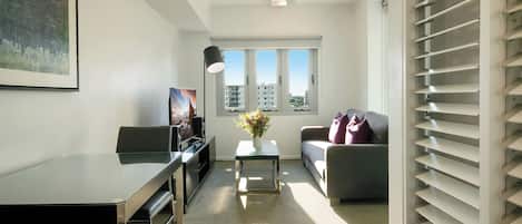 A modern living room with a glass-top table, a sofa, a TV, and a ceiling fan.