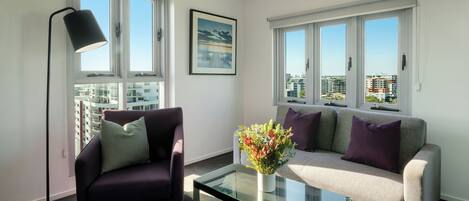 A modern living room with a sofa, armchair, floor lamp, and a glass coffee table with a floral arrangement.