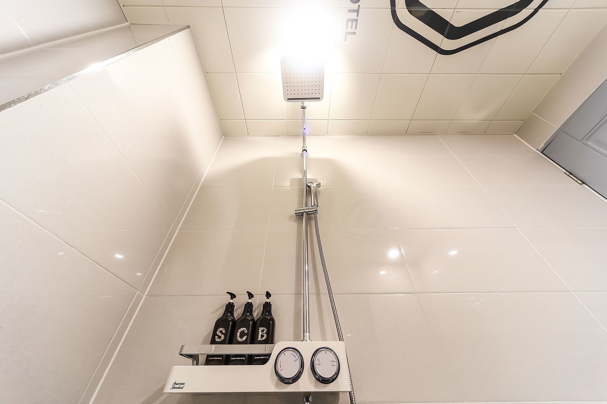 Une salle de bain moderne équipée d’une douche, d’un sèche-mains et de trois bouteilles de shampoing.