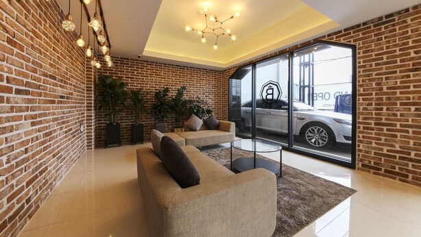 Un salon moderne avec un mur en briques, un canapé, une table basse et une grande fenêtre donnant sur l’extérieur, où l’on peut voir une voiture.