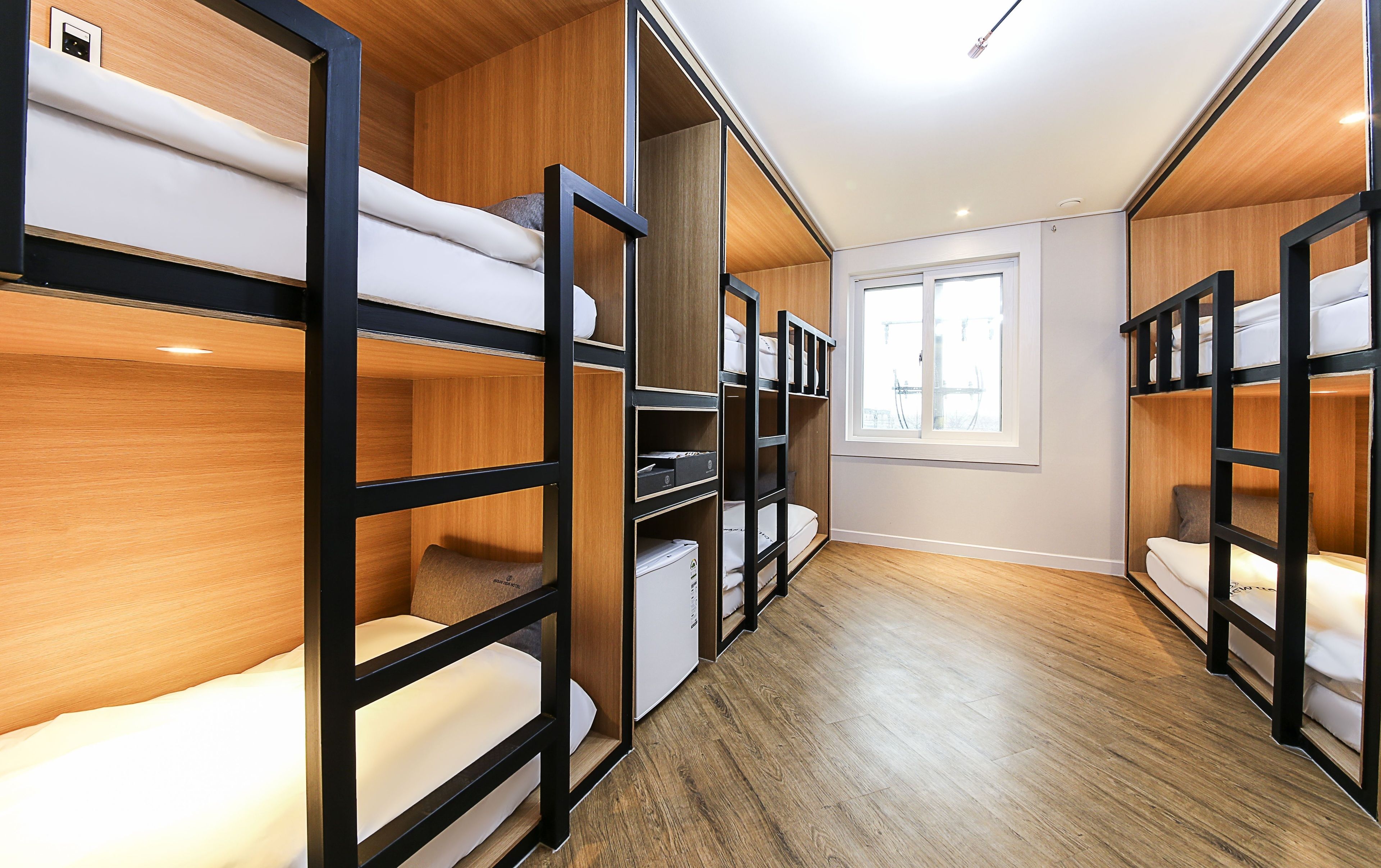 A hotel room with bunk beds, wooden flooring, and a window providing natural light.