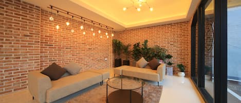 Una sala de estar moderna con paredes de ladrillo, dos sofás, una mesa de centro de vidrio y una lámpara en el techo.