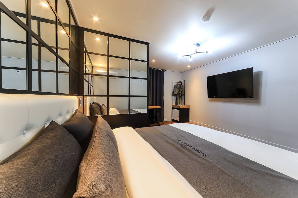 Ein modernes Schlafzimmer mit einem großen Bett, einem an der Wand befestigten Fernseher und einer Treppe mit Glastrennstäben.
