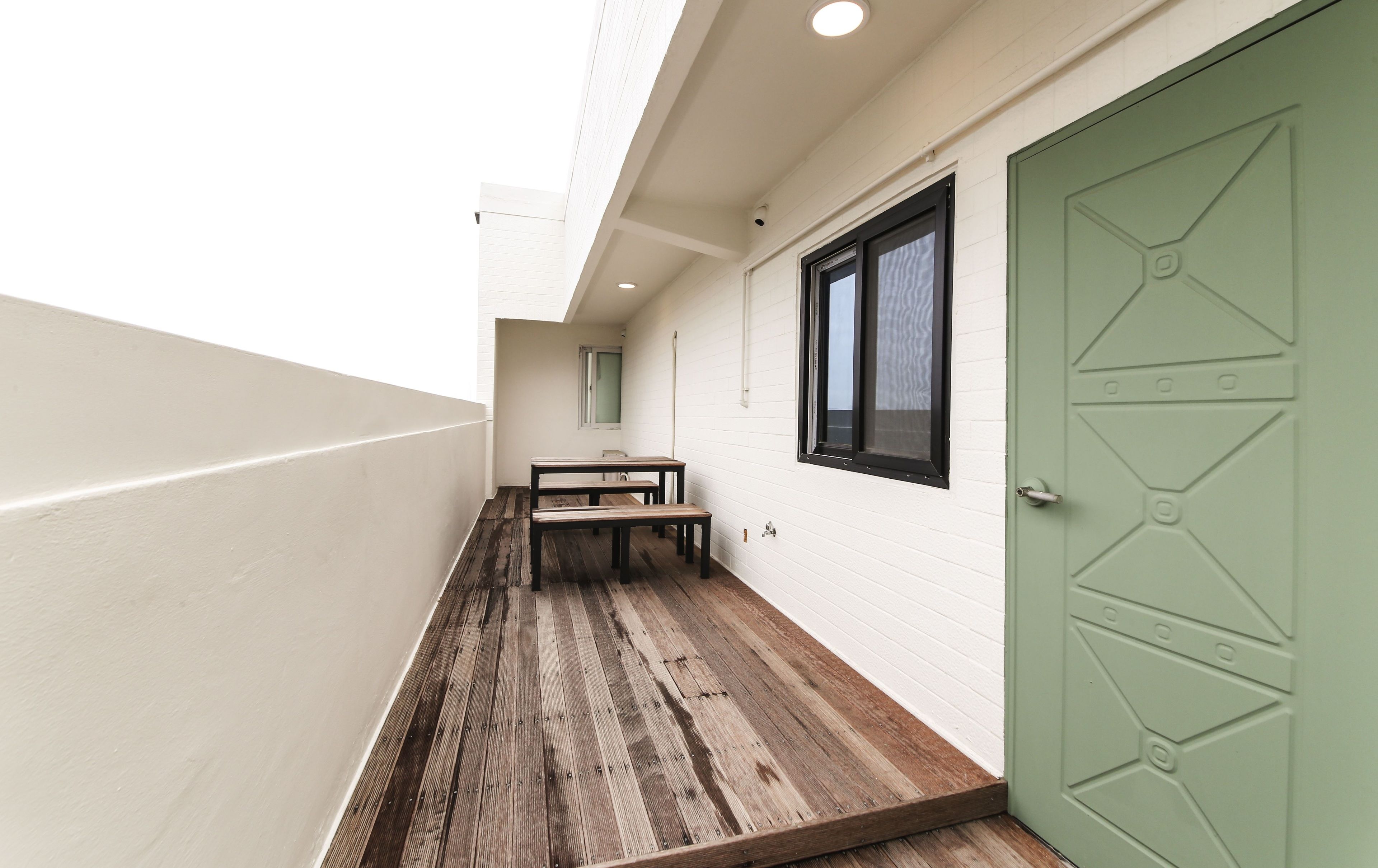 A narrow corridor with a wooden floor, a green door, and a window with a black frame.