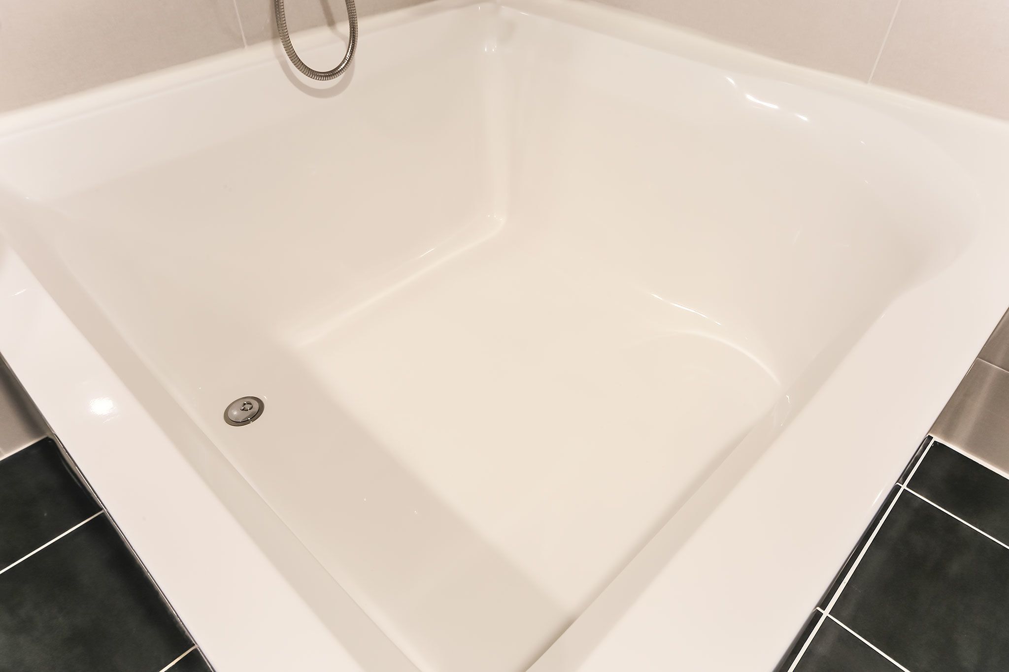 Une baignoire blanche avec un pommeau de douche, entourée de carreaux noirs et blancs.