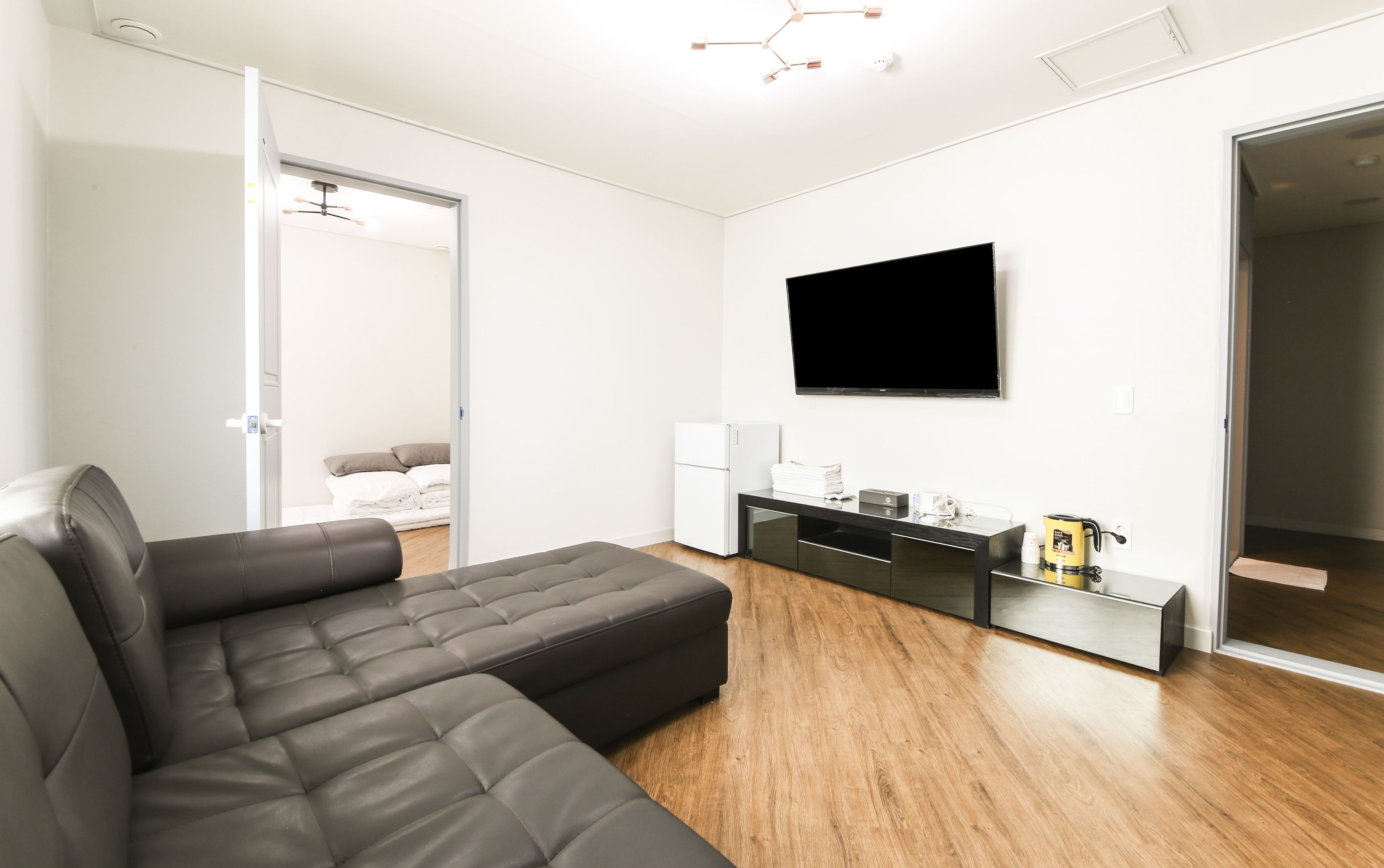 Een moderne woonkamer met een modulaire bank, een flatscreen televisie, een koffiezetapparaat en een kleine koelkast.
