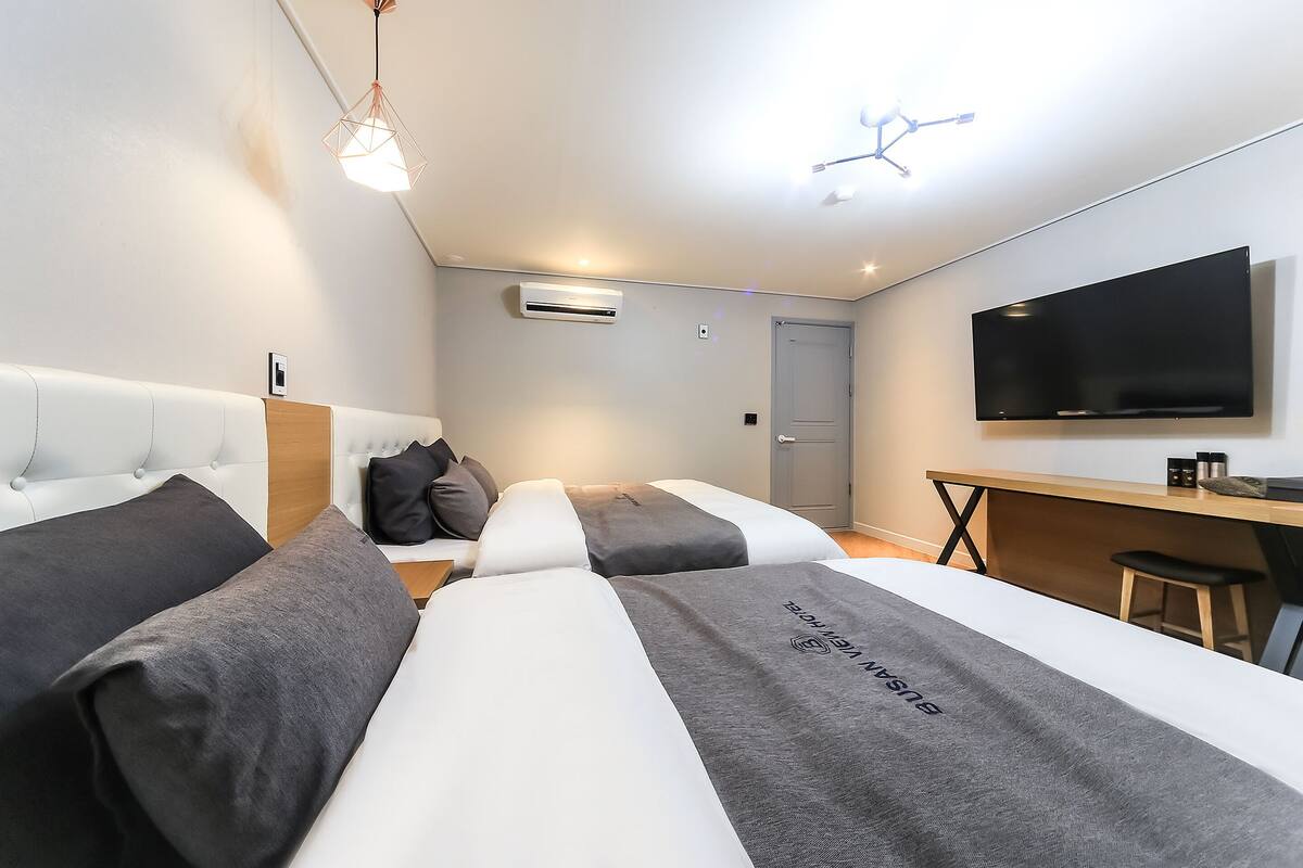 Ein modernes Hotelzimmer mit zwei Betten, einem Schreibtisch, einem Fernseher und einer Hängelampe.