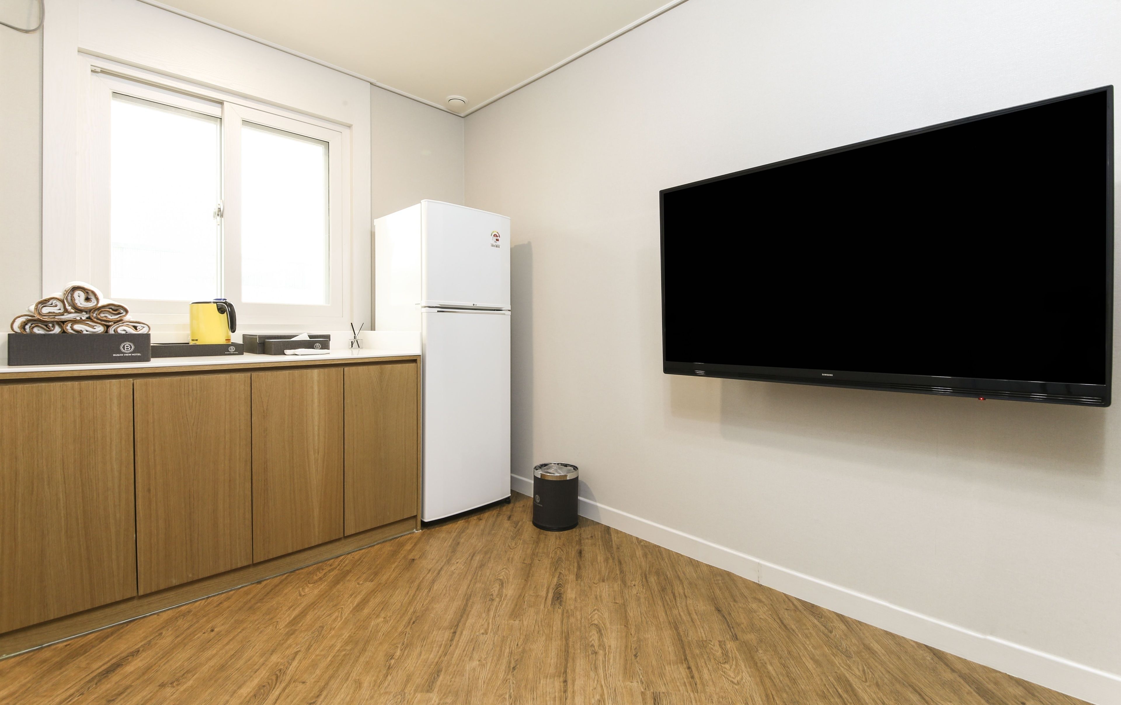 Una cocina moderna con armarios de madera, un refrigerador blanco, un bote de basura negro y un televisor montado.