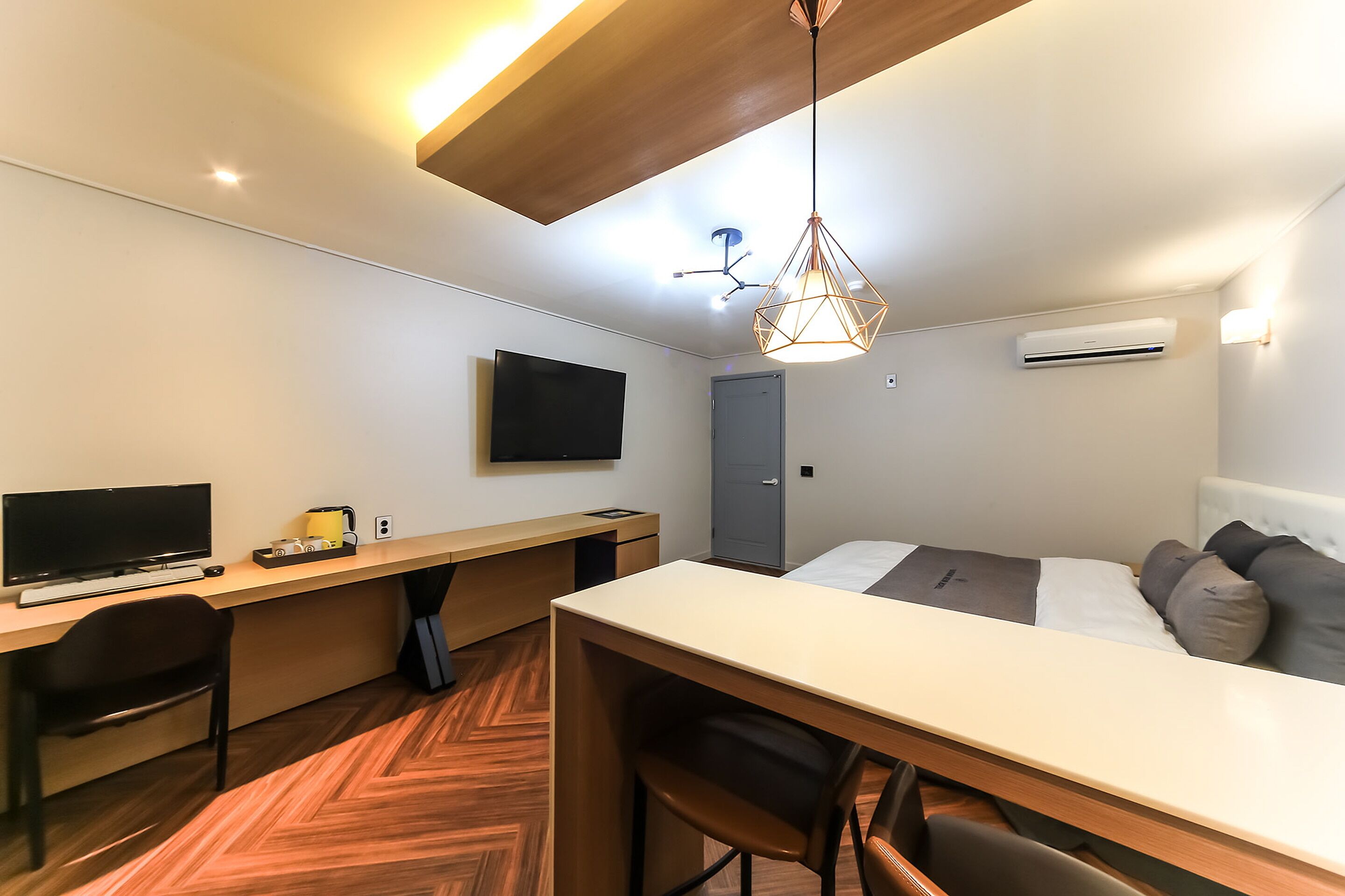 Een moderne hotelkamer met een houten bureau, een bed met kussens, een televisie en een airconditioner.