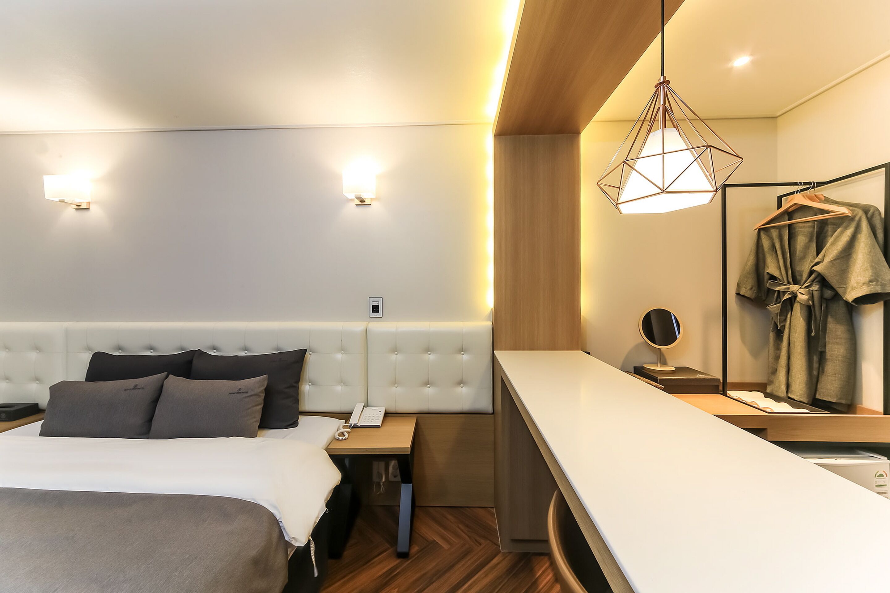 A modern hotel room with a large bed, bedside table, and a built-in bench.