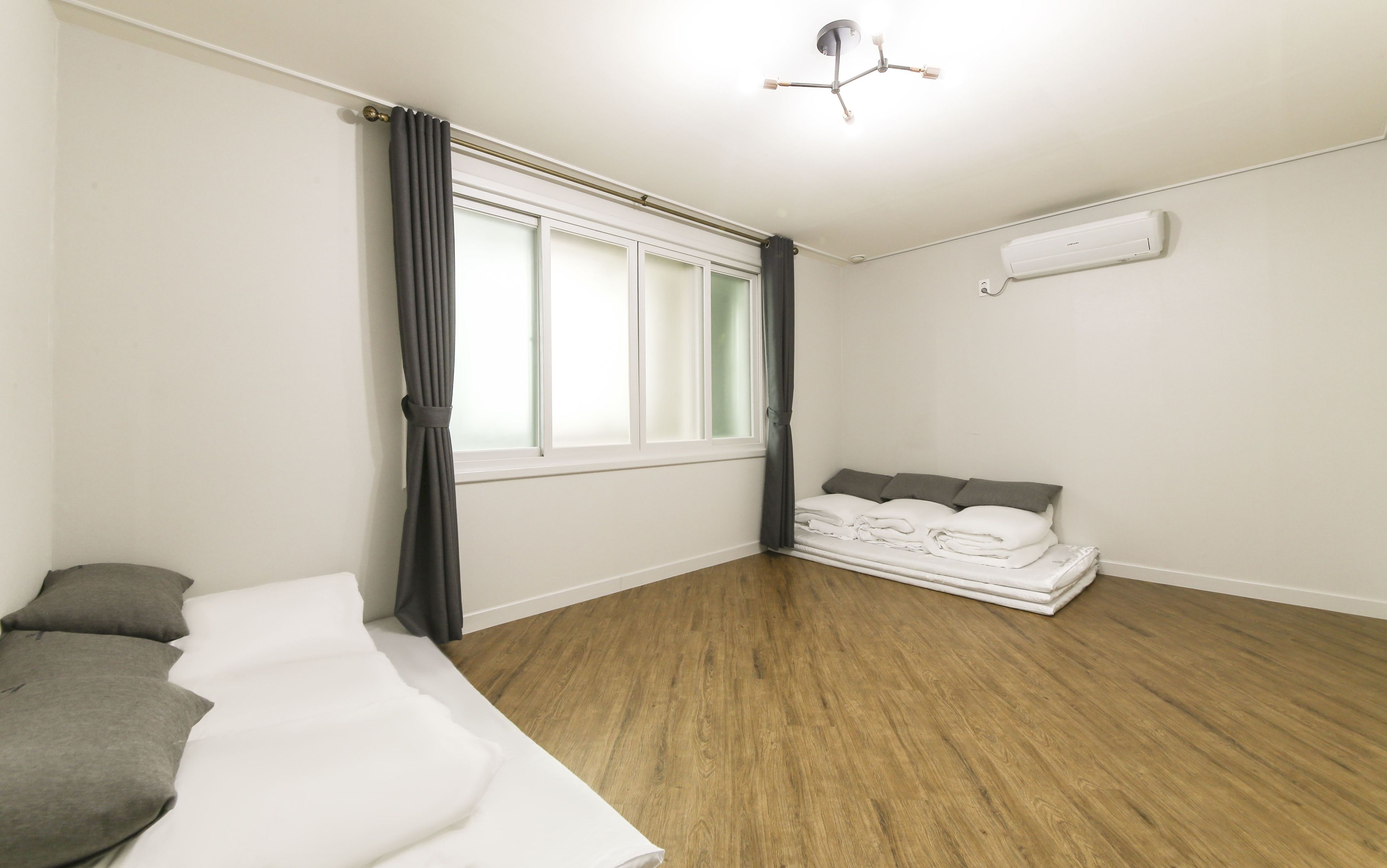 Une chambre à coucher avec un lit, une fenêtre avec des rideaux, un luminaire au plafond et un appareil de climatisation.