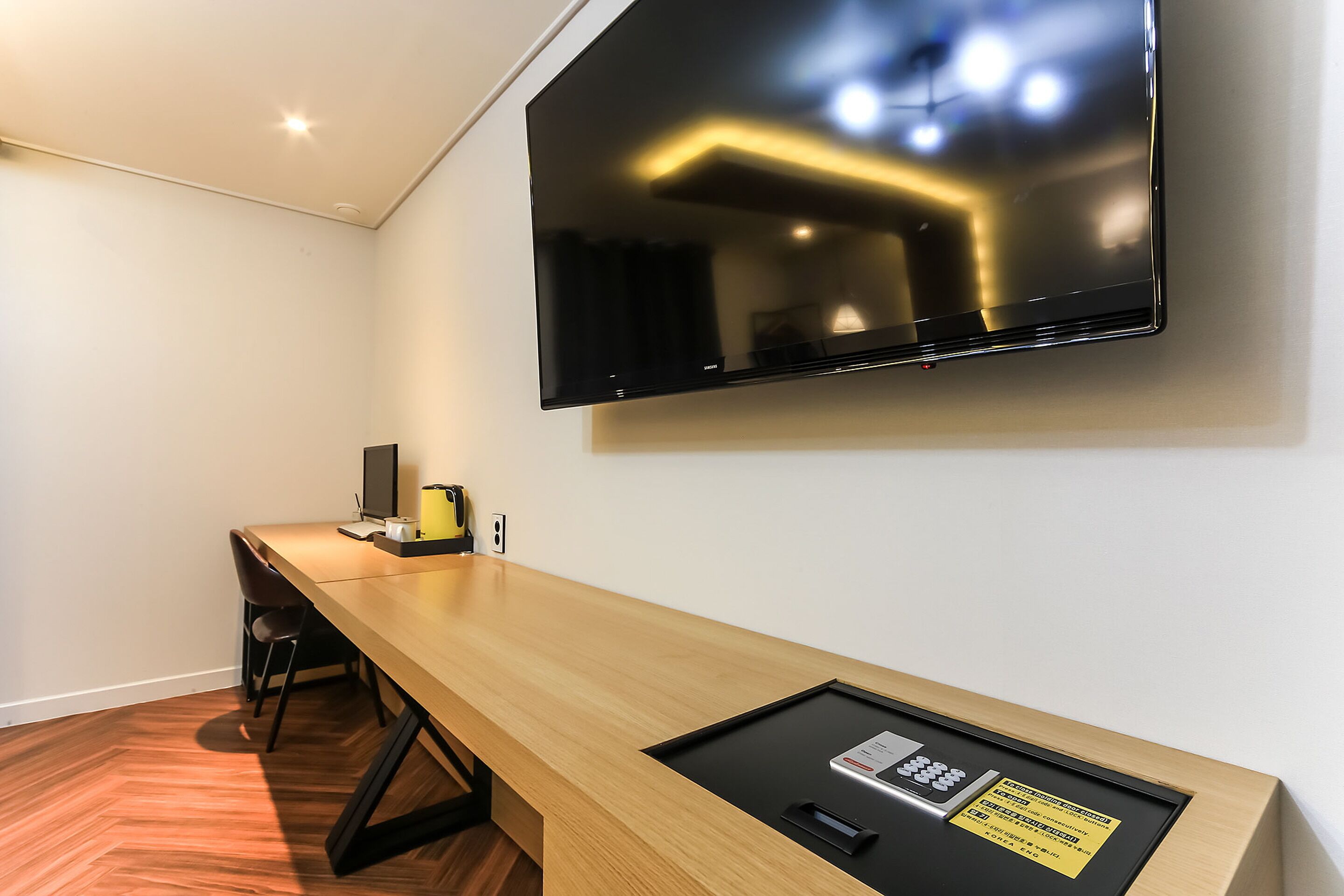 Una habitación de hotel moderna con un escritorio de madera, un televisor de pantalla plana montado en la pared y una mesita con un control remoto.