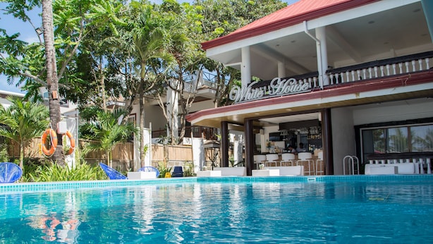 Une piscine avec un bâtiment blanc en arrière-plan, des arbres et un poste de surveillance pour les sauveteurs.
