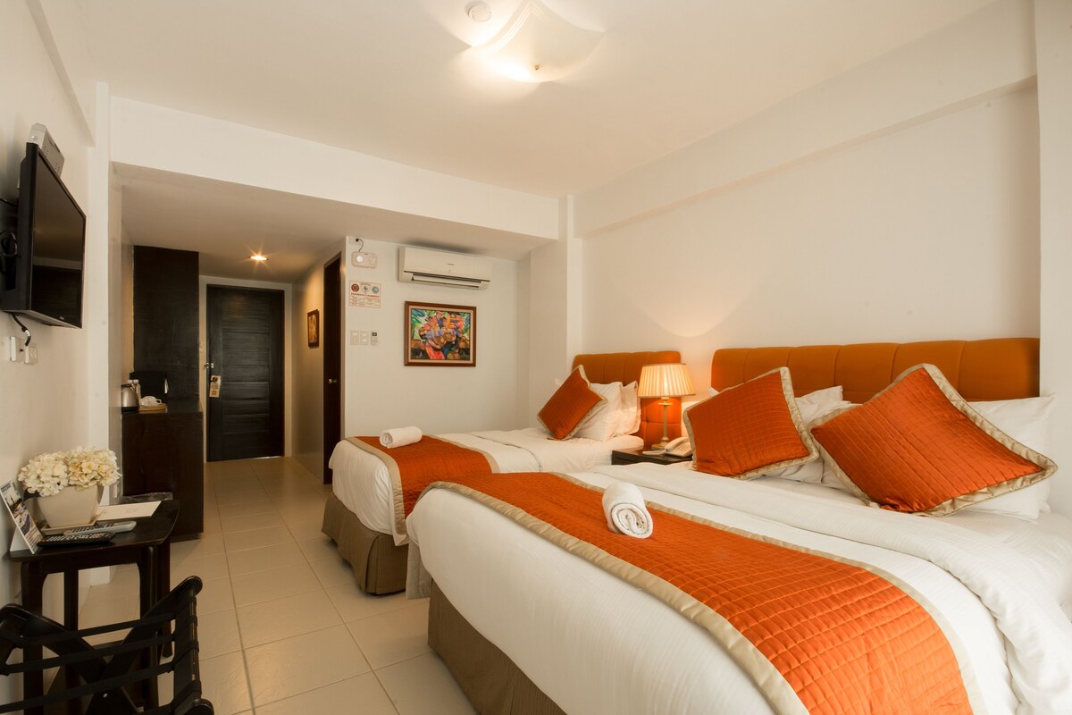 Une chambre d’hôtel avec deux lits, un bureau avec une chaise, une télévision et un appareil de climatisation.
