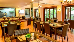 Un restaurant doté de nombreuses tables et chaises, d’un téléviseur fixé au mur et de grandes fenêtres offrant une vue sur la verdure.