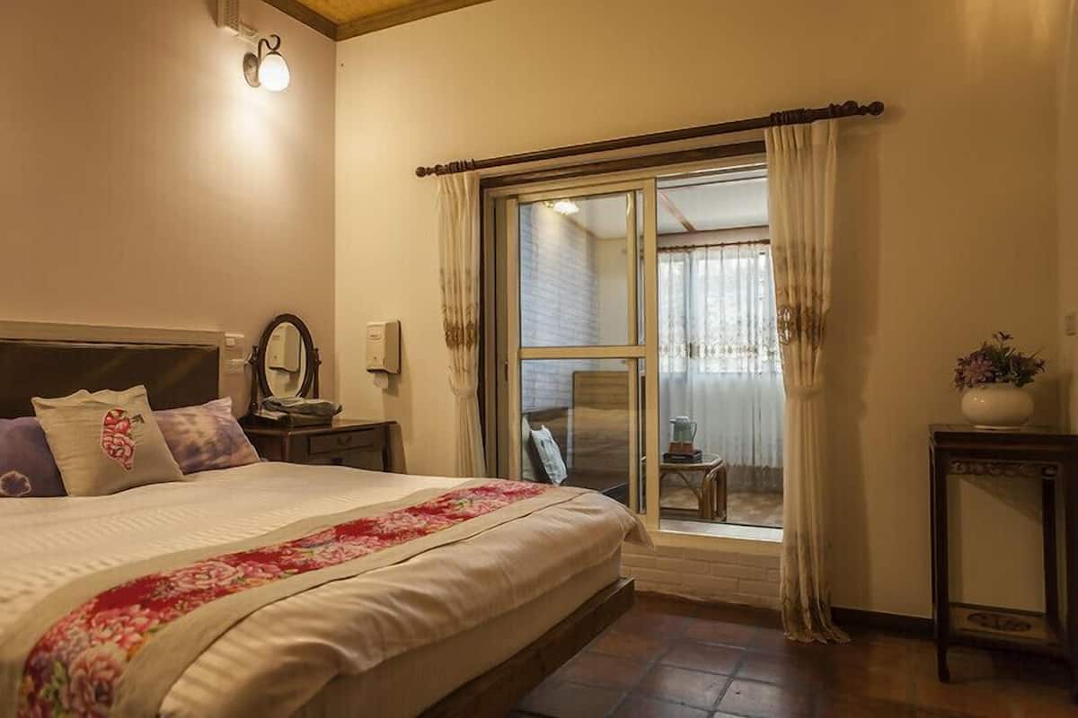 Un dormitorio con cama, mesita de noche, cortinas y vistas al exterior.