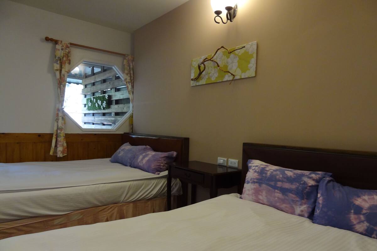 Habitación de hotel con dos camas, ventana con vistas, una obra de arte en la pared y una mesita de noche con lámpara.