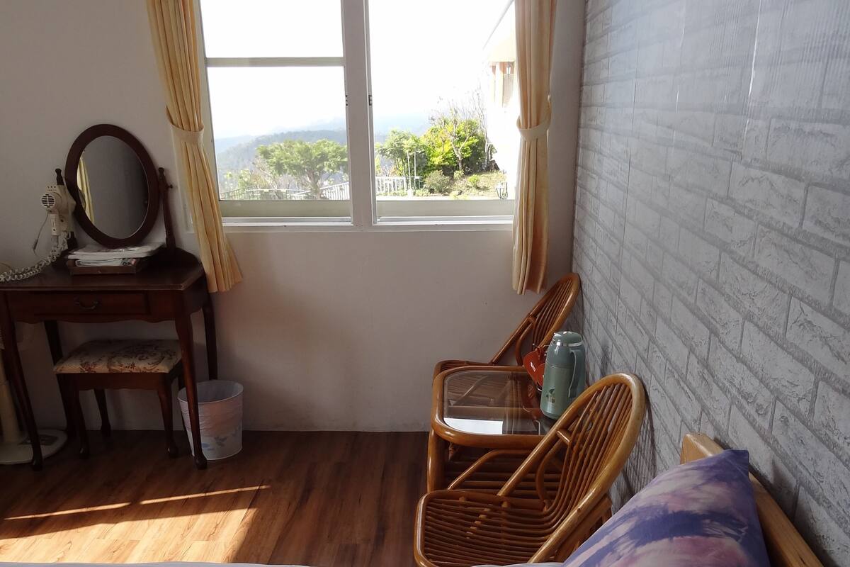 Un dormitorio con una cama, un aparador de madera con espejo, una silla y una ventana con cortinas.