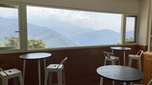 Una habitación con amplios ventanales que ofrecen vistas a la montaña, paneles de madera y varias mesas redondas con sillas.