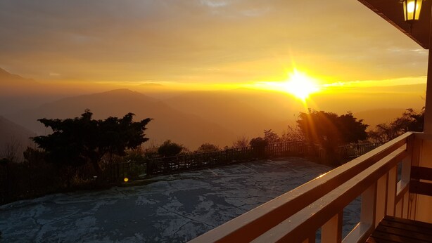 Un balcón con vista a una puesta de sol sobre un paisaje montañoso.