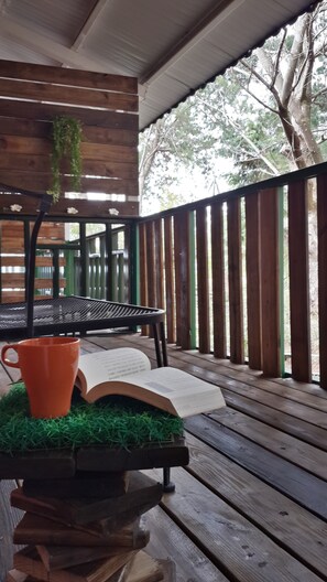 Una terraza de madera con un banco, una mesa con un libro y una taza, y una planta colgante.