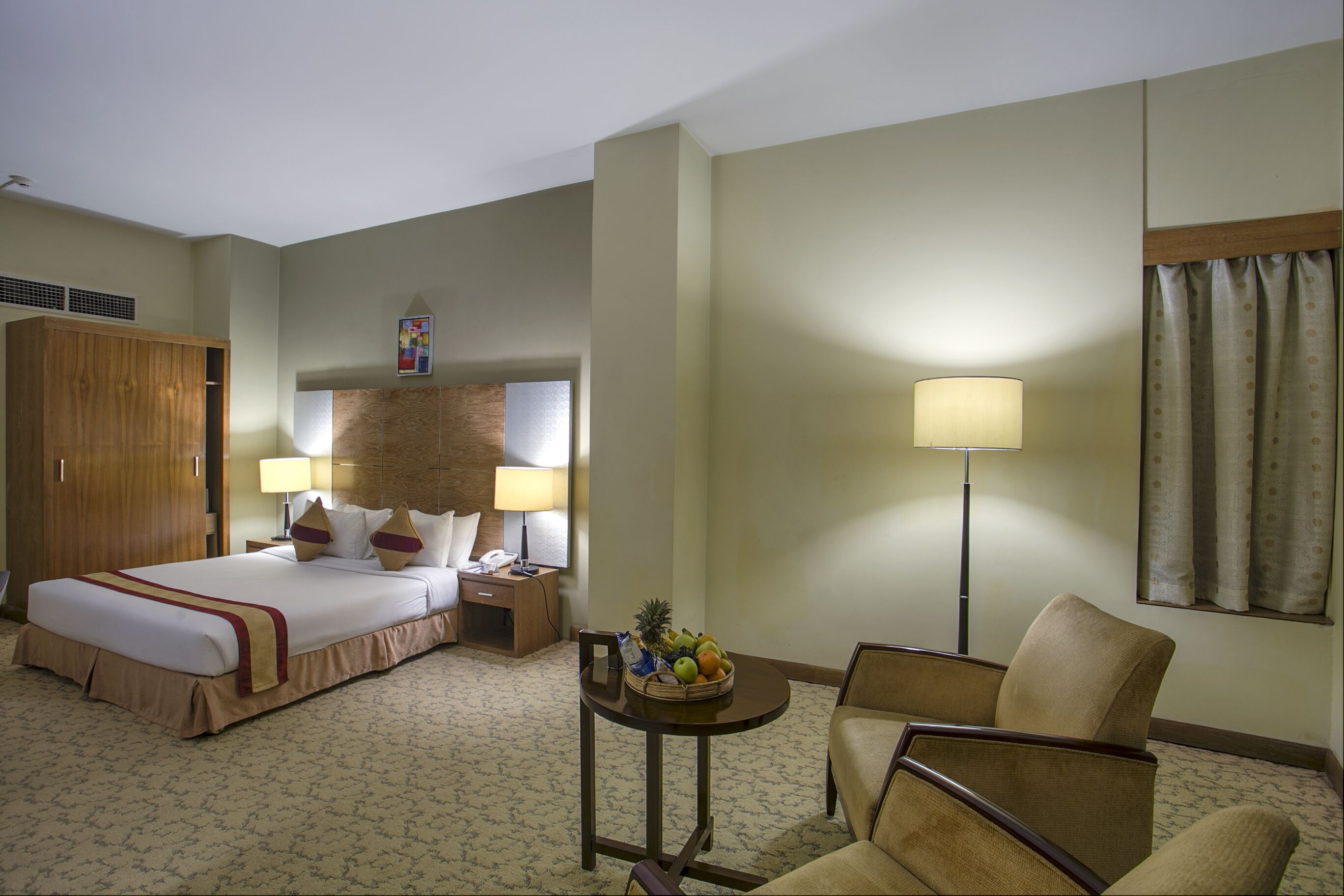 Une chambre d’hôtel avec un lit, une table de chevet, une lampe, une chaise et une petite table sur laquelle se trouvent des fruits.