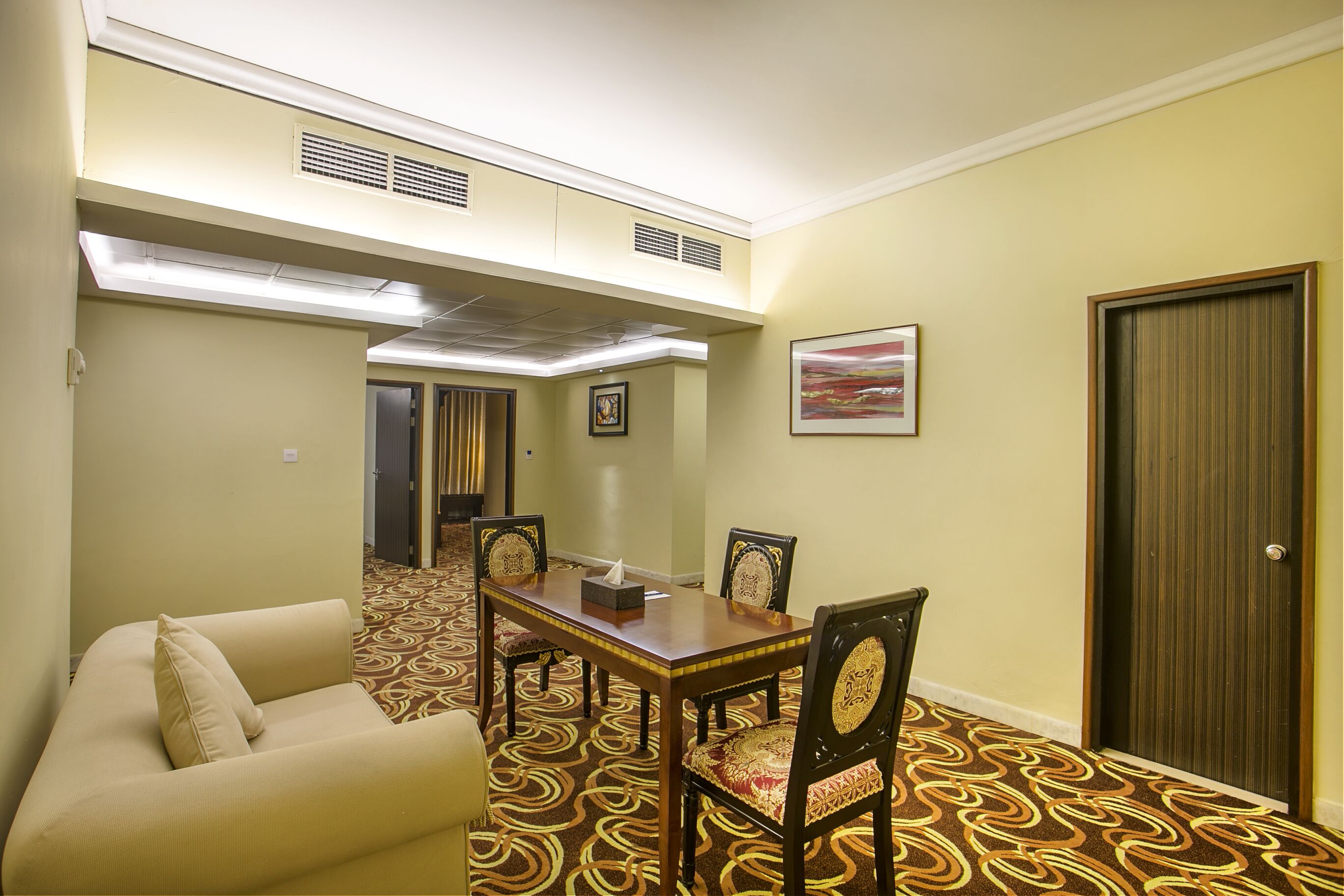 A conference room with a wooden table and chairs, a sofa, and a patterned carpet.