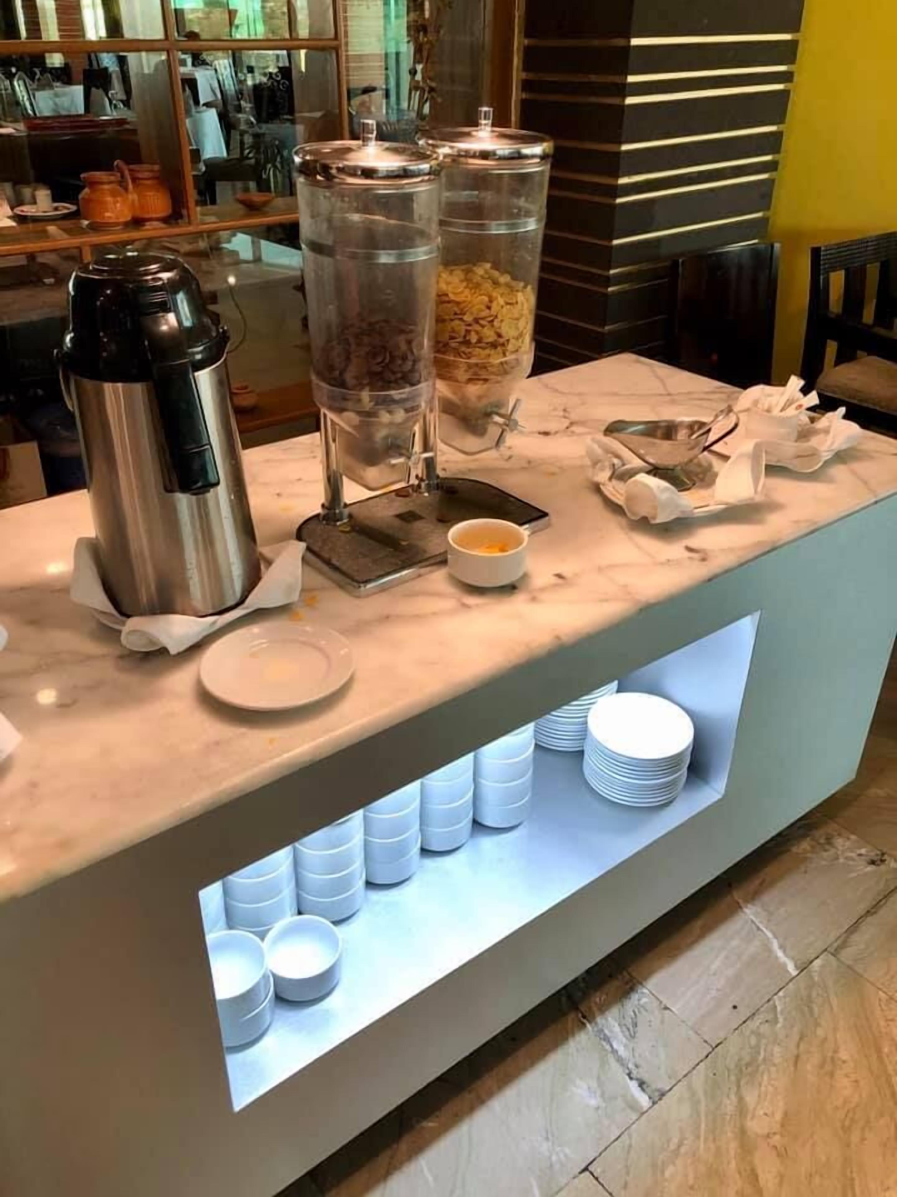 A breakfast bar with a coffee maker, two dispensers, and a bowl of cereal.