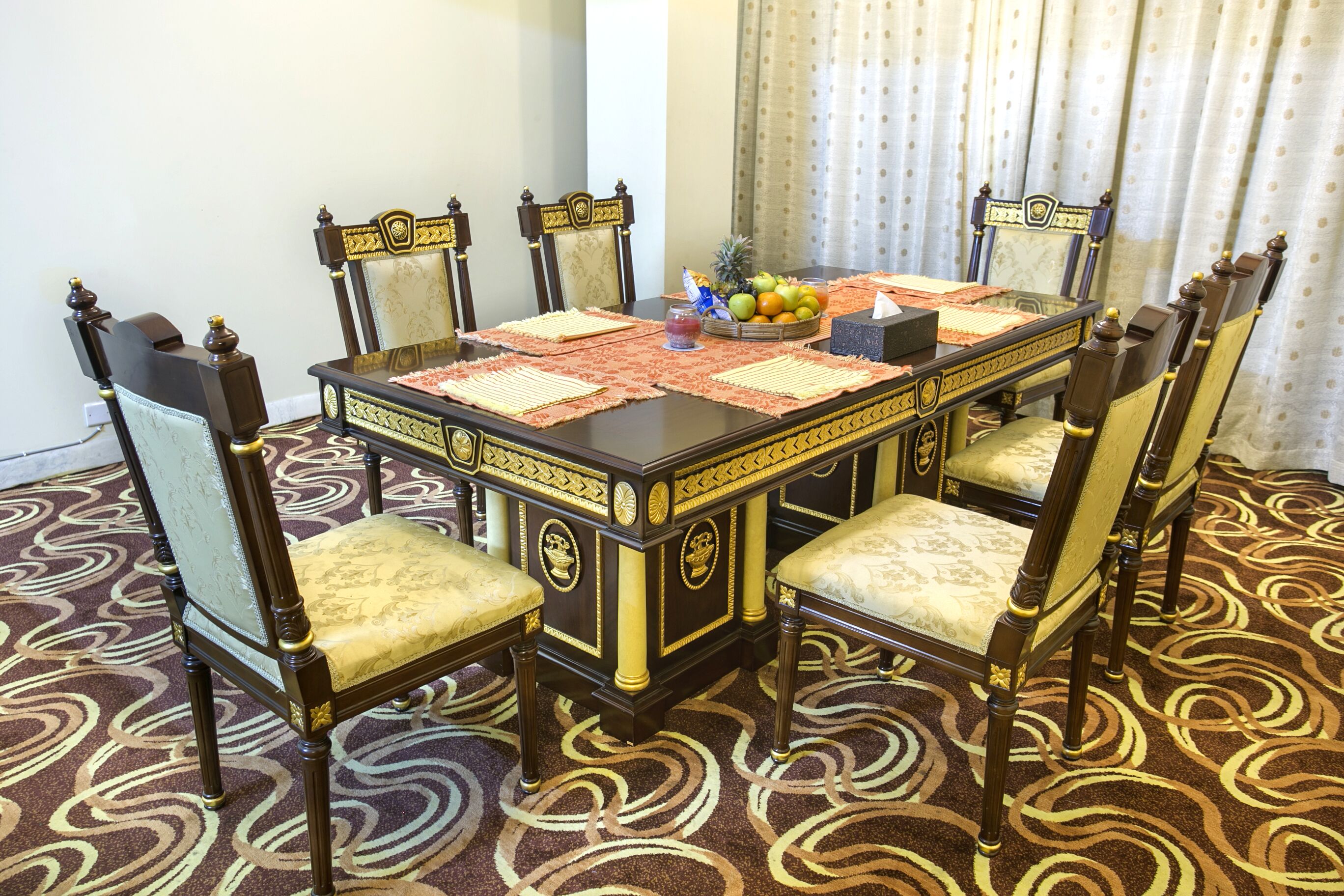 A formal dining room with a large table, ornate chairs, and a patterned carpet.
