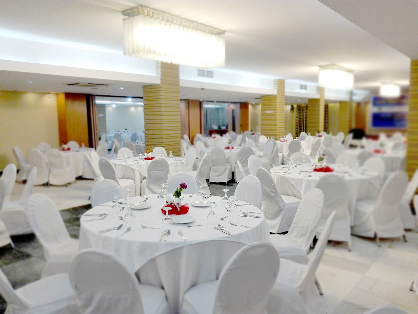 A banquet hall with round tables set for dining, white chairs, and a chandelier.