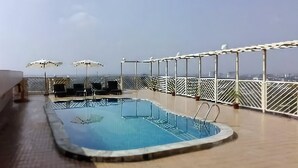 A rooftop pool with two sun loungers and umbrellas, surrounded by a white railing and a view of the city skyline. - Rose View Hotel (Sylhet)