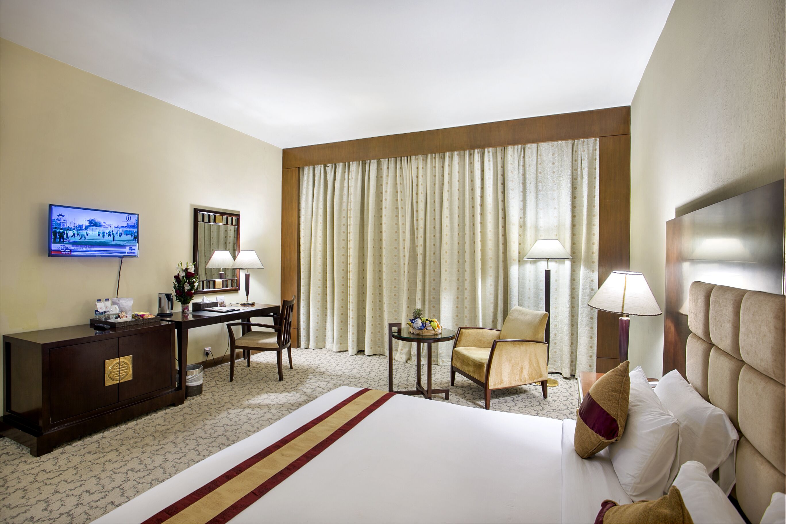 A hotel room with a bed, a desk, a television, and a window with curtains.